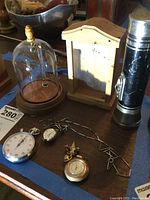 Two wooden watch display cases, a black Eveready flashlight, stopwatch, two women's watches (one on a chain, one pin watch) laid out on a wooden table.