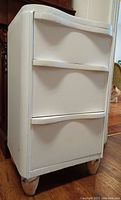Front view of white wooden bedside table with two curved drawers and round wooden legs.