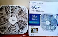 Front view of the 20 inch Classic box fan next to its original packaging box. Shows fan's model name, features, and its circular speed control dial.