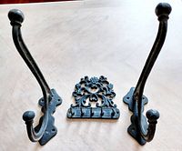 Two cast iron coat hooks with rounded ends and one decorative cast iron key hanger placed on a wood surface.