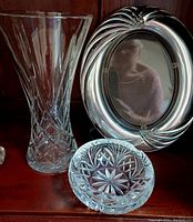 Crystal vase, glass picture frame with rounded swirl border, and round cut crystal dish on a wood surface