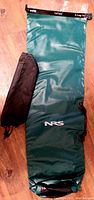 Full view of green NRS dry sack with labeled logo and included storage pouch beside it on wooden floor.