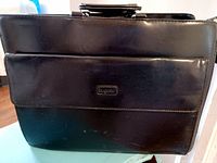 Front view of the black Bugatti leather briefcase showing the flap with Bugatti logo and minor wear marks on the leather.