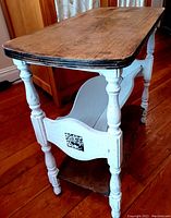 Side angled view showing the two-tone finish with brown stained top and bottom shelf, white painted and sanded legs and side panels, and the decorative black and white detail.