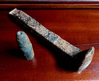 Rust-covered railway spike and bullet placed on wooden surface, showing surface texture and patina.