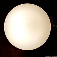 Front view of the lamp showing the round white illuminated diffuser with some slight scuff marks.