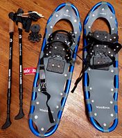 Pair of WindRiver snowshoes with bindings and two WindRiver trekking poles with interchangeable tips and baskets laid out on wooden floor.