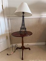 View of wood round accent table with metal Eiffel Tower lamp on top.