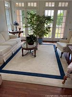 Full view of rectangular cream and blue bordered area rug in living room