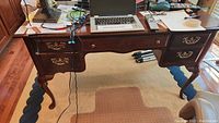Full frontal view of Bassett desk showing top surface with items (not included), six drawers, carved legs, brass handles, and carpet underneath.
