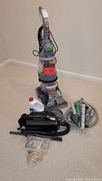 Hoover carpet cleaner upright with accessories and cleaning solution in front on carpet.