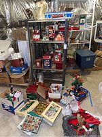 Wide view of metal shelf and surrounding floor area showing multiple Christmas decorations and boxes including figurines, ornament sets, and collections.