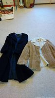 Two coats lying on carpet: black lamb coat and brown/white faux shearling coat