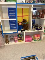 Photo of white shelving unit with Madeline doll, Scooby Doo plush, giraffe figurine, merry-go-round toys, small pink house, and assorted dolls and figurines arranged on shelves.