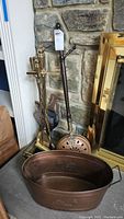Fireplace tools set with stand and copper coal scuttle beside a stone fireplace and brass fireplace screen.