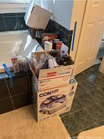 Conair Foot Spa in box underneath a cardboard box with various personal care products including men's cologne, hair products, and lotions.