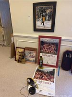 Full view showing framed Pittsburgh Steelers football player photo on wall (not included), two framed Redskinettes posters propped on floor, and three pieces of moose artwork also on floor.