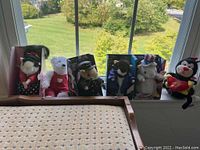 Front view of six plush animals including bears in various costumes and a musical ladybug plush on a window ledge.