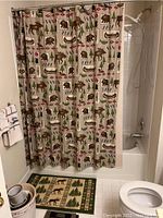 View of the bathroom shower curtain with animal and nature pattern, along with matching rug, part of toilet and bathroom fixtures visible.