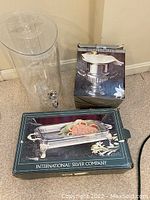 Photo showing all three items: clear acrylic beverage dispenser, boxed silver champagne ice bucket, and boxed silver casserole holder with International Silver Company branding.