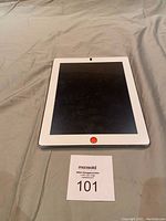 Front view of the Apple iPad 2 showing the white bezel and black screen with an orange sticker over the home button.