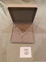 Full view of necklace and earrings set displayed inside an open beige velvet hinged jewelry box.