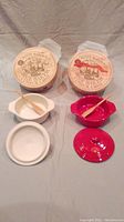 Opened Petite Maison brie baker showing ceramic inserts in white and red, each with matching wooden spreader spoons
