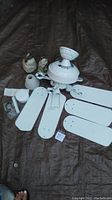 Photo showing all white ceiling fan parts laid out on a dark tarp including motor housing, four blades, glass light covers, and mounting hardware.