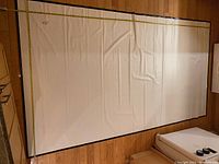 Full view of white screen laid flat on wood floor with tape measures showing width and height