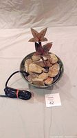 Front view of the copper decorative fountain with real rocks and pump cord in a round basin.
