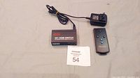 Top view of the HDMI switch box with power adapter and remote control placed on white surface, showing product label '3X1 HDMI SWITCH'.