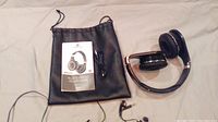 Bluetooth headphones with carrying pouch, manual, and USB cable, folded on a white background
