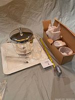 Photo showing silver-tone ice bucket with lid, handles, metal tongs, white tray, one glass tumbler, and additional glasses wrapped in original packaging in cardboard box.