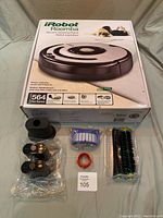 Front view of iRobot Roomba 564 Pet Series box alongside new battery, docking station, replacement filter, cleaning brush and brush roller.