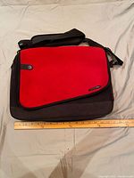 Front view of the neoprene messenger bag with a red flap and black body, showing button detail and label.