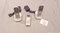 Three Panasonic cordless phones displayed with two charging bases and two power adapters. One phone is without a base.