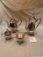 Full set assembled with lids on teapot and coffee pot, showing shiny reflective surfaces and ornate handles and feet.