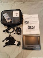 All included components of the portable DVD player lot laid out on flat surface including the player, remote, power adapter, straps, carrying case, and instruction sheet.