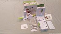 Overview of Spiralizer Deluxe Kit parts laid out on fabric surface, showing main unit, blades, hand guard, and other attachments.