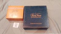 Photo of the Trivial Pursuit Genius Edition dark blue box alongside the orange Genius expansion pack box both showing front top sides.