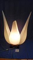 Front view of lamp illuminated showing five white acrylic petal panels and dark wood base