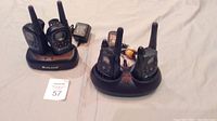 Two sets of black Midland walkie talkies placed in their charging docks with power adapters visible, all resting on a beige cloth.