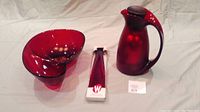 Red salad bowl and utensils in original packaging, red coffee carafe thermos, and red chips and dip bowl all-in-one on beige backdrop.