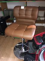 Side angle view of the brown barstool showing padded seat and backrest with chrome swivel base and footrest, placed indoors on hardwood floor.