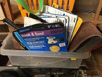Plastic container with assorted sanding and abrasive supplies including Norton Hook & Sand discs