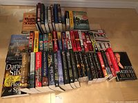 Full lot of novels by Bernard Cornwell, Daniel Silva, Lee Child, and others stacked on a wooden surface.