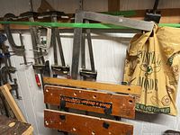 Overall view of assorted clamps hanging on a wall above and near a foldable Black & Decker Workmate with wooden tops and metal folding legs.