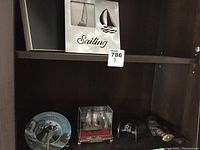 Photo of shelf with sailing-themed picture frames, 3D metal sailboats, turtle ship in display case, small cannon, and cutting tool in scabbard