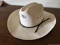 Cream colored cowboy hat with black strap, large/extra large size, on a wooden surface, shot from above and side angle