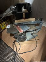 Full view of the Delta 15 inch scroll saw showing the blade area, motor, table surface, power cord, and extra blades placed on the table.